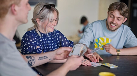 Three students playing a card game at a table