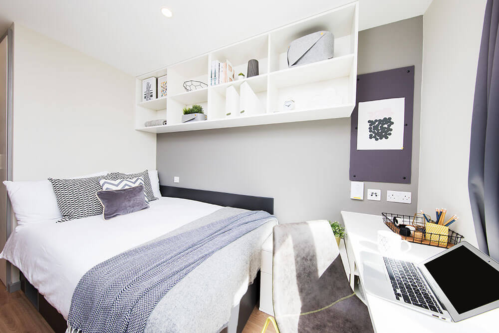 Bedroom in student accommodation with bed, shelves and desk